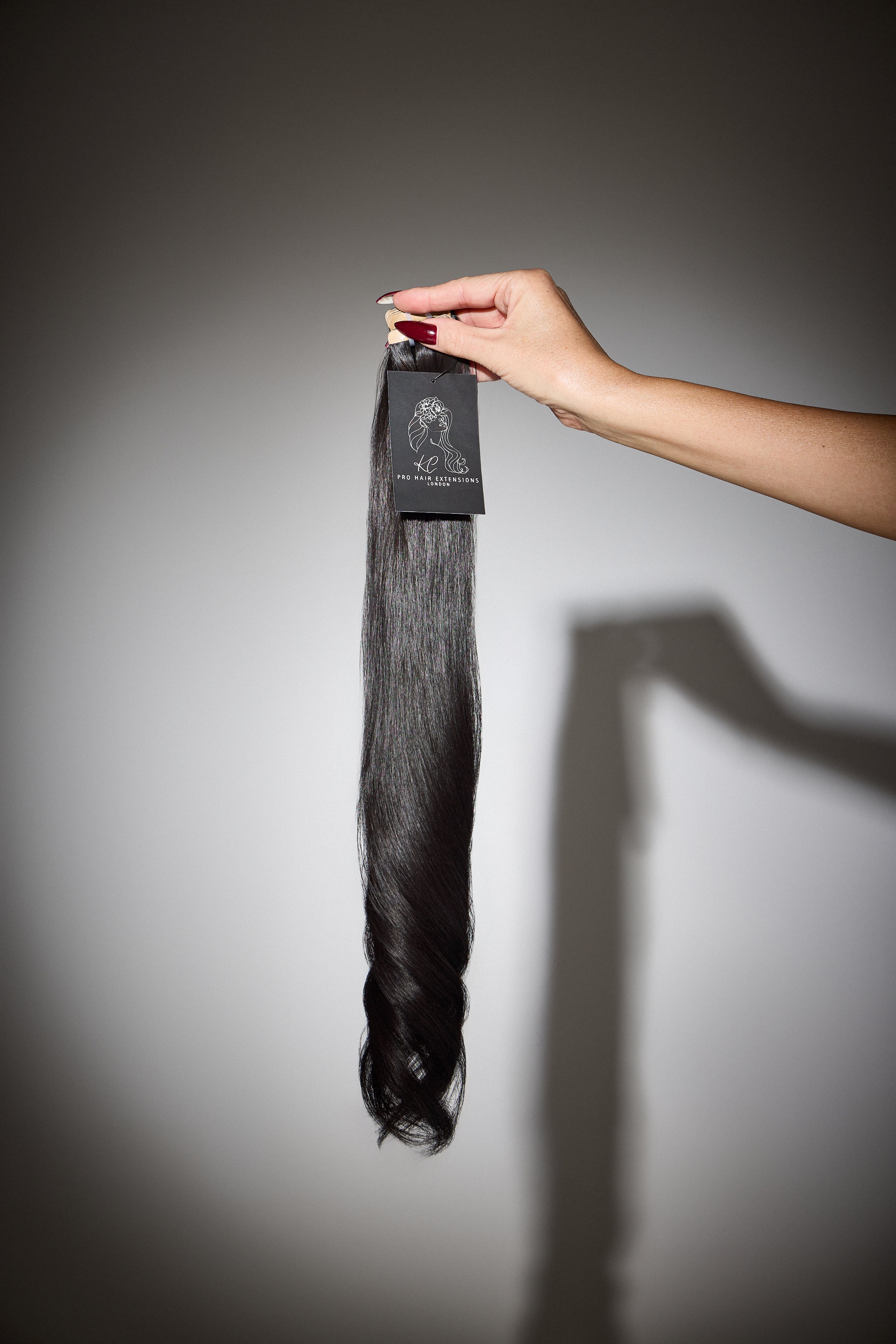 Hand holding a bundle of black hair extensions with a label against a gray background