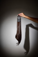 Hand holding a hair extension against a gray background