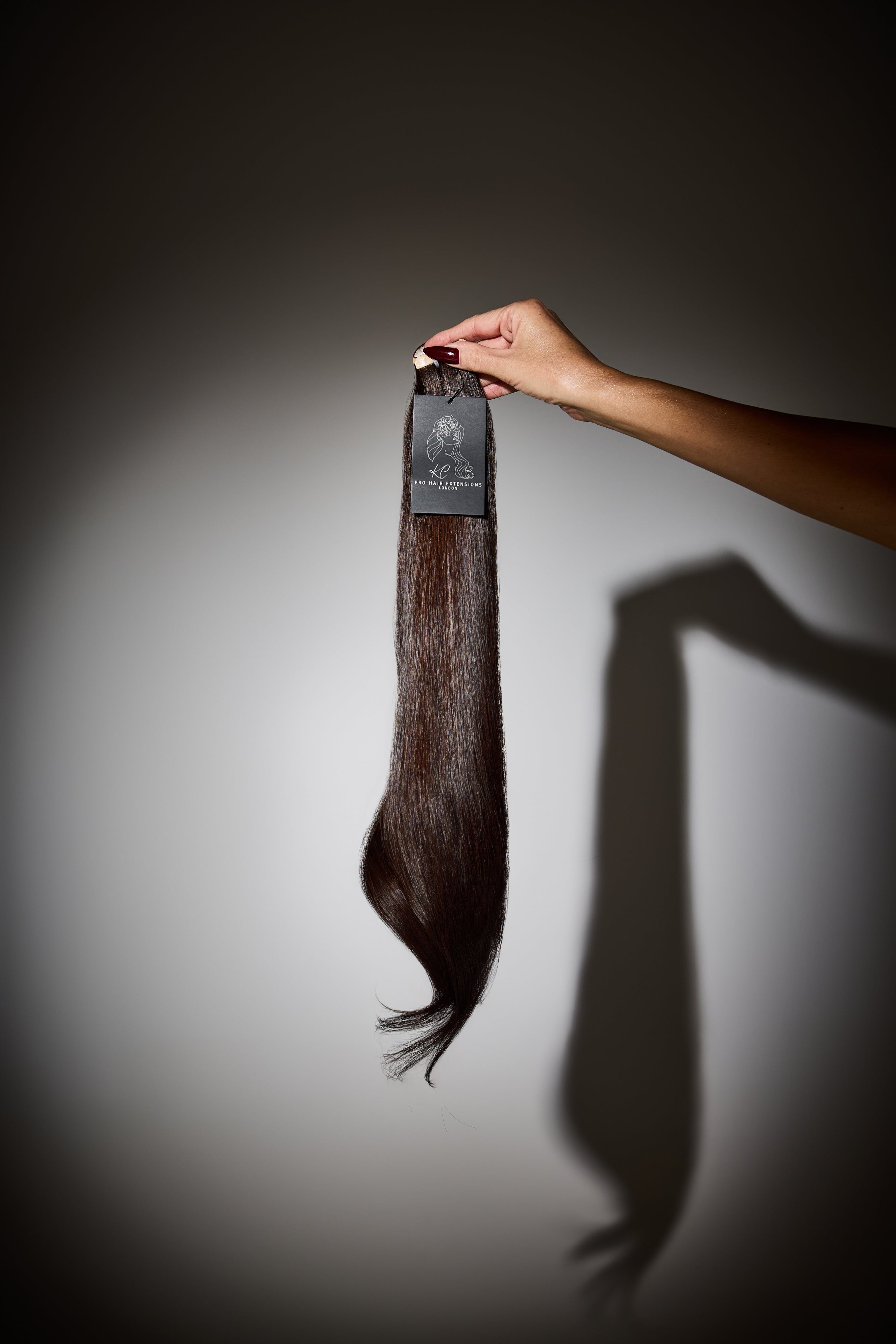 Hand holding a hair extension against a gray background